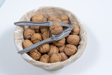 basket with whole walnuts and nutcracker on a white background, top view