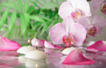 SPA concept. Rose petals, burning candles and orchid flowers with water reflection