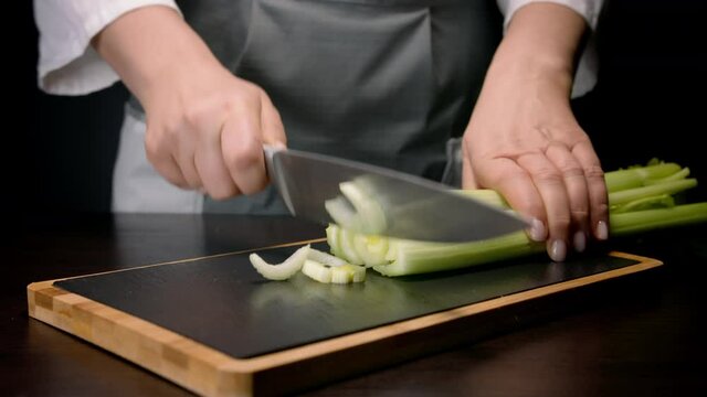 Female hands cutting in pieces celery stalk with kitchen knife. Close up