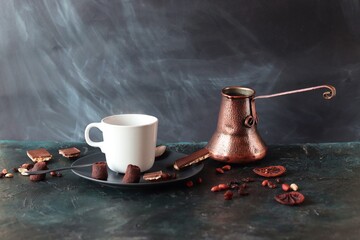 Cup with hot coffee, copper coffee maker, chocolate and spices on the table, dark background, home kitchen
