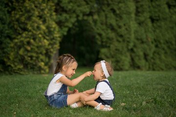 Two funny girls play in the park on the lawn and feed each other with blades of grass. The sisters play and frolic in the park on the grass.