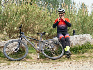 Male cyclist puts on his helmet in nature next to his mountain bike