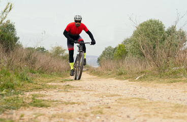 Male cyclist pedaling down a dirt road with a mountain bike. Effort, competition