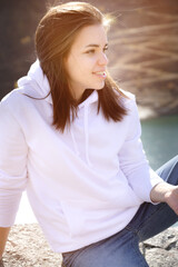 Attractive cute young caucasian woman sitting on stones in the mountains against the background of a high mountain lake on a sunny day