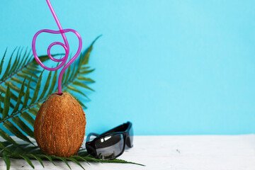 A coconut with straw and black sunglasses on blue background. Summer and trave concept. copy space