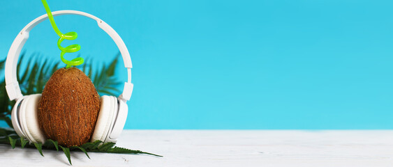 A coconut with straw and headphones on blue background. Summer and trave concept. copy space. banner