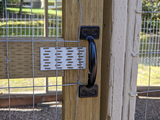 view of a black door handle on a chicken coup on a large farmland © ColleenMichaels