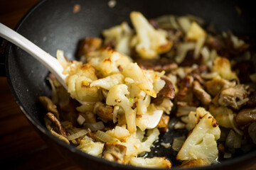 fried cauliflower with wild porcini mushrooms and onions in a pan