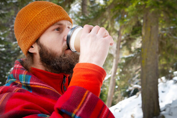 bearded man drinking from a paper cup with a blanket on his shoulders