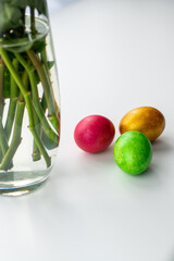 Vase with flowers and Easter eggs on a white table.