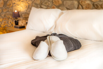 Cama blanca de hotel con conjunto de batín y zapatillas para ducha - obrazy, fototapety, plakaty