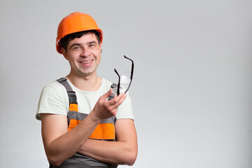 Young cheerful,carefree builder constructor in hard hat and overalls on studio background, building industry concept