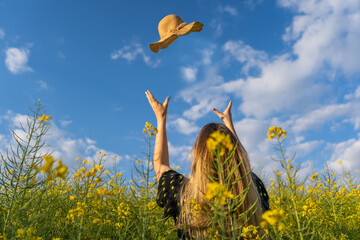 Happy young woman throwing her straw sun hat in a yellow flowers field.Spring lifestyle,summer sunny day concept, copy space.