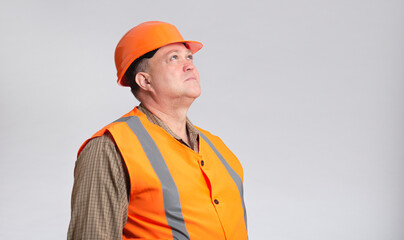 portrait of middle-aged building contractor in hard hat and reflective vest looking up on grey studio background, building industry concept