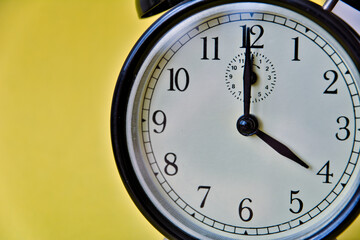 Shot of vintage retro analog clock on yellow background showing 4 o clock
