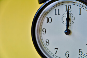 Shot of vintage retro analog clock on yellow background showing 12 o clock
