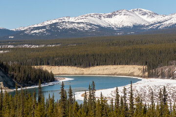 Winding Yukon River outside of Whitehorse in spring time with wonderful scenic view of the wilderness surrounding snow capped mountain peaks in the background. Desktop wallpaper, tourism, visit. 