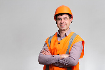 Portrait of smiling young construction worker in hard hat and reflective vest on grey studio background, successful engineer