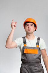 Young construction worker in hard hat and reflective vest raised finger up as sign he has new idea on studio background