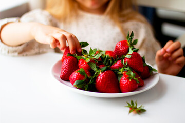 Cute little girl eating fresh strawberry in the kitchen. Healthy vitamin snack for kids. Ripe fresh berries. Harvest season. Natural vitamins .