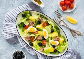 American version of Nicoise salad with canned tuna, boiled potatoes and green asparagus beans in an oval white dish on a gray concrete plate.