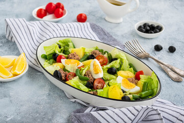 American version of Nicoise salad with canned tuna, boiled potatoes and green asparagus beans in an oval white dish on a gray concrete plate.