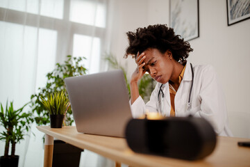 Displeased black healthcare worker using computer and reading an e-mail at doctor's office.