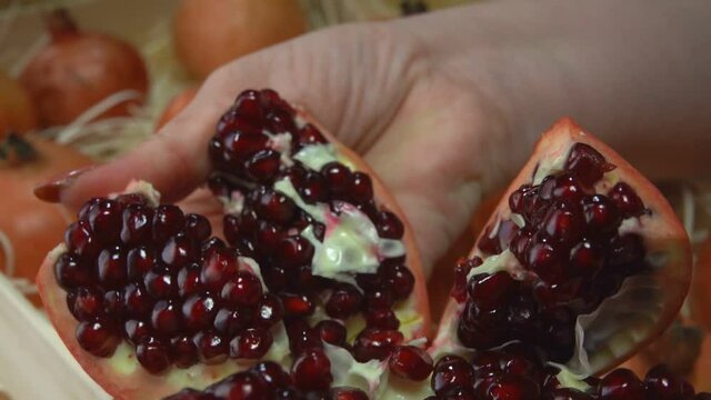 Female hands are breaking a juicy ripe pomegranate into the six pieces on the background of the box full of pomegranates