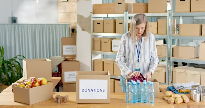 Mature Caucasian pretty female warehouse worker volunteer working in shipping delivery charitable stock organization packing donations box. Donating and volunteering, charity center concept.