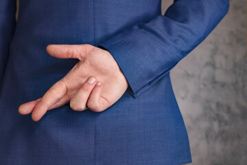 Man in blue business suit holding crossed fingers behind back. gray background