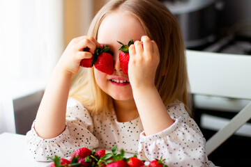  Cute little girl eating fresh strawberry in the kitchen. Healthy vitamin snack for kids. Ripe fresh berries. Harvest season. Natural vitamins .