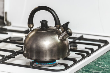 A metal dark kettle with a whistle heats the water to a boil on a gas stove in the kitchen