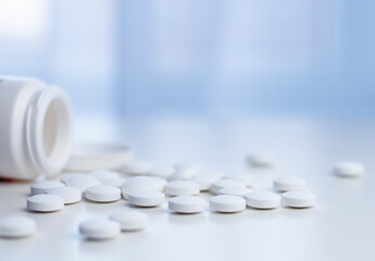 medicine bottle with cap and white pills on the white table and blue window