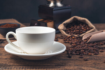 An empty white ceramic cup against the background of coffee beans and a coffee grinder.