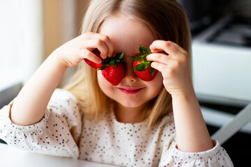 Cute little girl eating fresh strawberry in the kitchen. Healthy vitamin snack for kids. Ripe fresh berries. Harvest season. Natural vitamins .