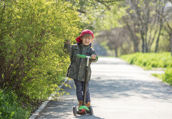 Fototapeta premium a beautiful boy rides a three-wheeled scooter on the sidewalk. Spring green background