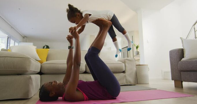 Happy african american mother and daughter doing yoga exercise at home