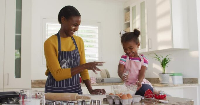Happy african american mother and daughter wearing aprons having fun while cooking in kitchen
