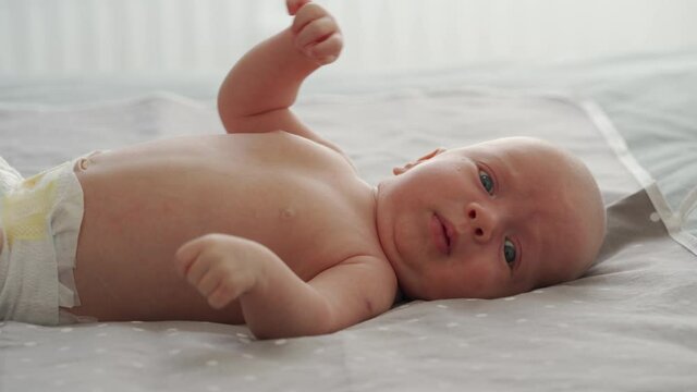 Mother with baby boy doing exercise simple exercises to make baby bones and muscles stronger, newborn infant lying on bed against the window. High quality 4k footage