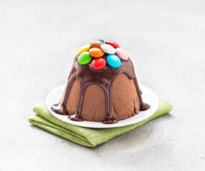 Cottage cheese chocolate dessert, poured with icing and decorated with colorful candies on a plate on a linen napkin on a light gray background. Easter