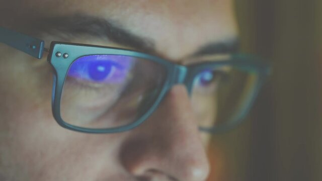 Close up portrait of a software engineer who is working: the eyes are focused on the screen, on the lens of the glasses we see the reflection. Vintage cine effect.