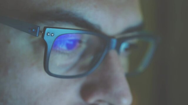 Close up portrait of a software engineer who is working: the eyes are focused on the screen, on the lens of the glasses we see the reflection. Vintage cine effect.