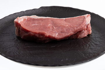 Sliced raw calf meat with a thin layer of fat around it on black handmade plate isolated on white
