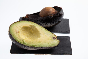 Fresh and ripe avocado next to rotting avocado cut in half with seed visible isolated on white