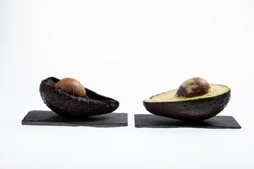 Fresh and ripe avocado next to rotting avocado cut in half with seed visible isolated on white