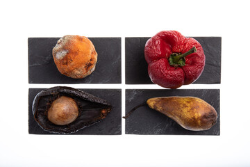 Group of different fruits and vegetables rotting and with mold on them placed on black slates