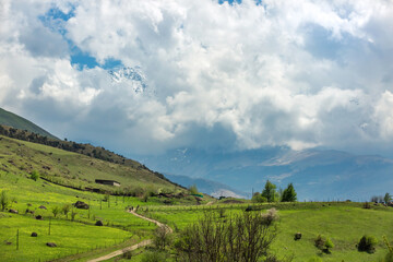 Fototapeta premium Rural landscape. Road, emerald hills, tractor. Farm fields in the mountains. Village in North Ossetia Alania, Russia. Fiagdon Gorge in sunlight.