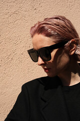 Vertical headshot of young stylish woman with pinkish hair, wearing sunglasses.