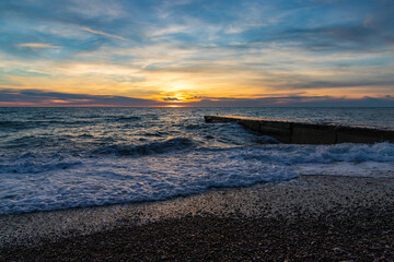 Obraz premium Beautiful sunset over the sea and stone pier with clouds and horizon on the beach in Sochi, Russia