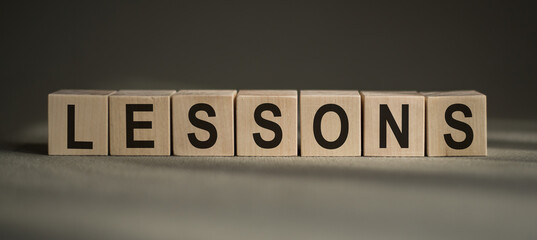 A wooden blocks with the word LESSONS written on it on a gray background.